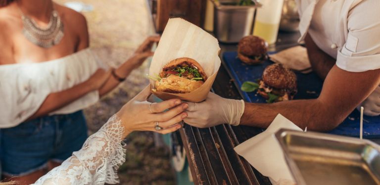 Woman hand reaching for a burger at food truck. Closeup of food truck salesman serving burger to female customer.